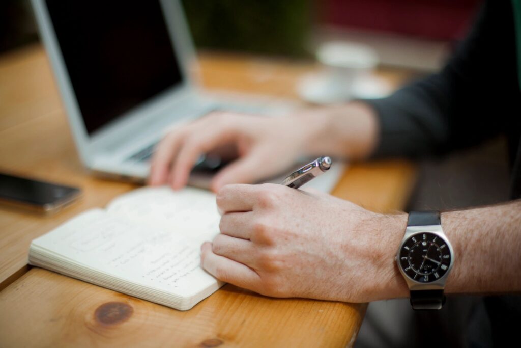 Photo of someone taking notes near a laptop computer